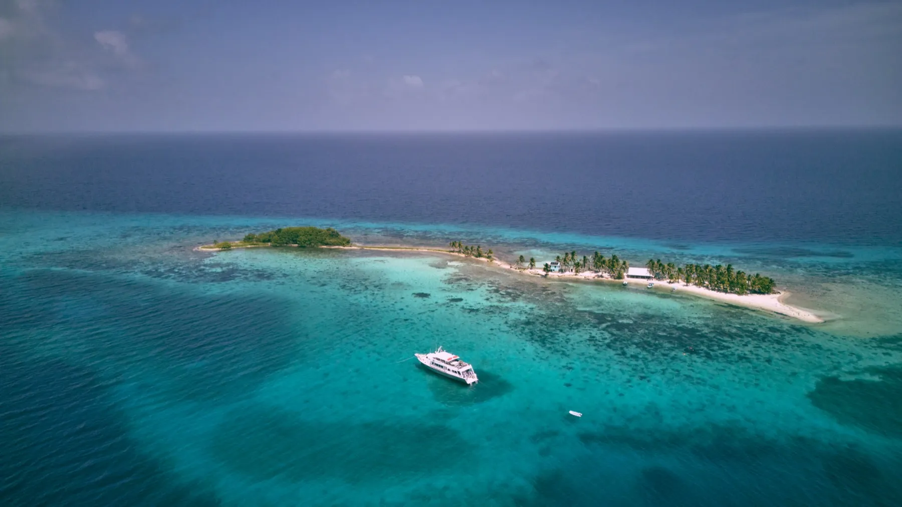 Aerial view of a small caye with a dive boat moored in turquoise water